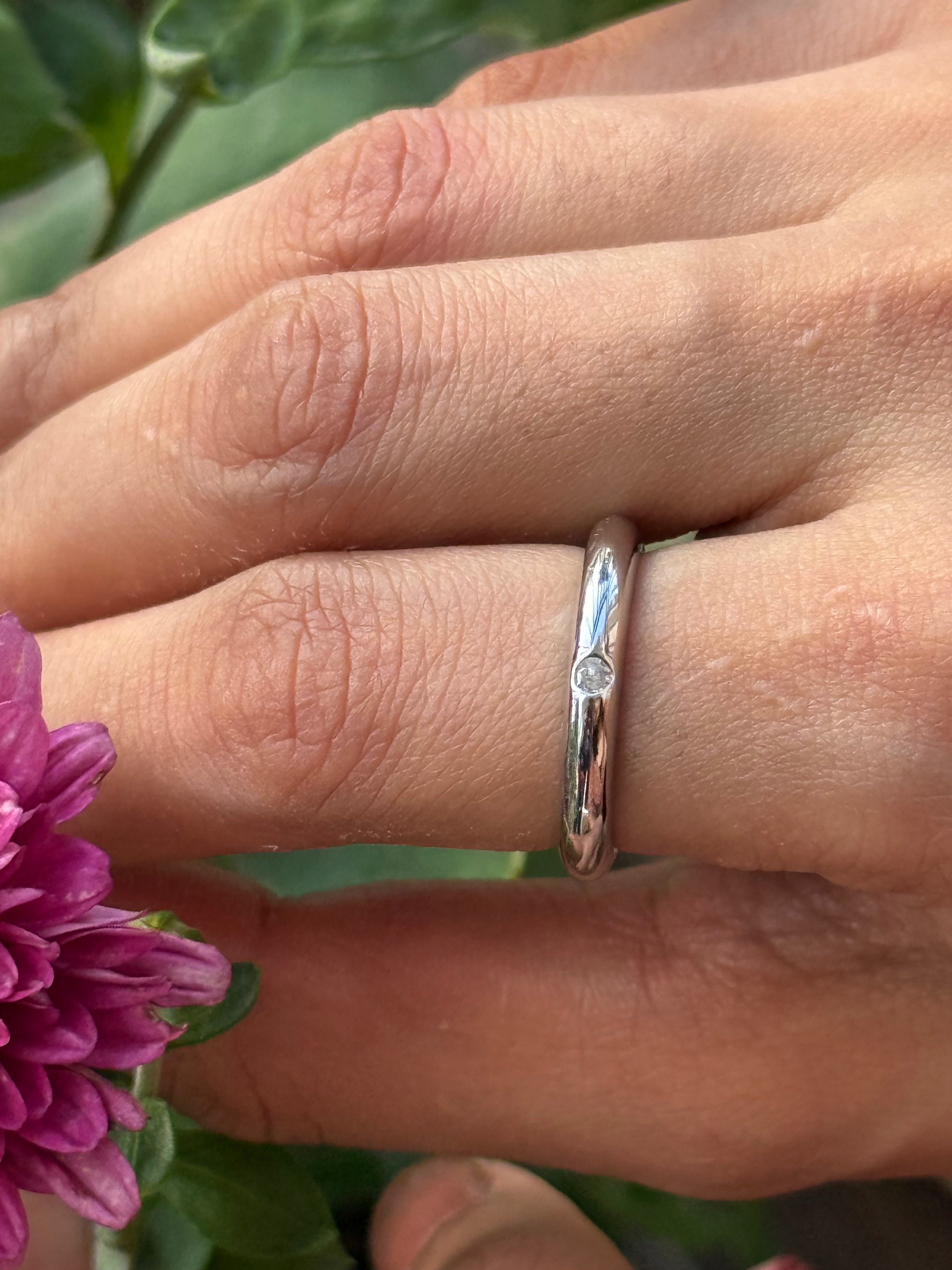Close-up of a hand wearing a silver ring with a purple flower in the foreground