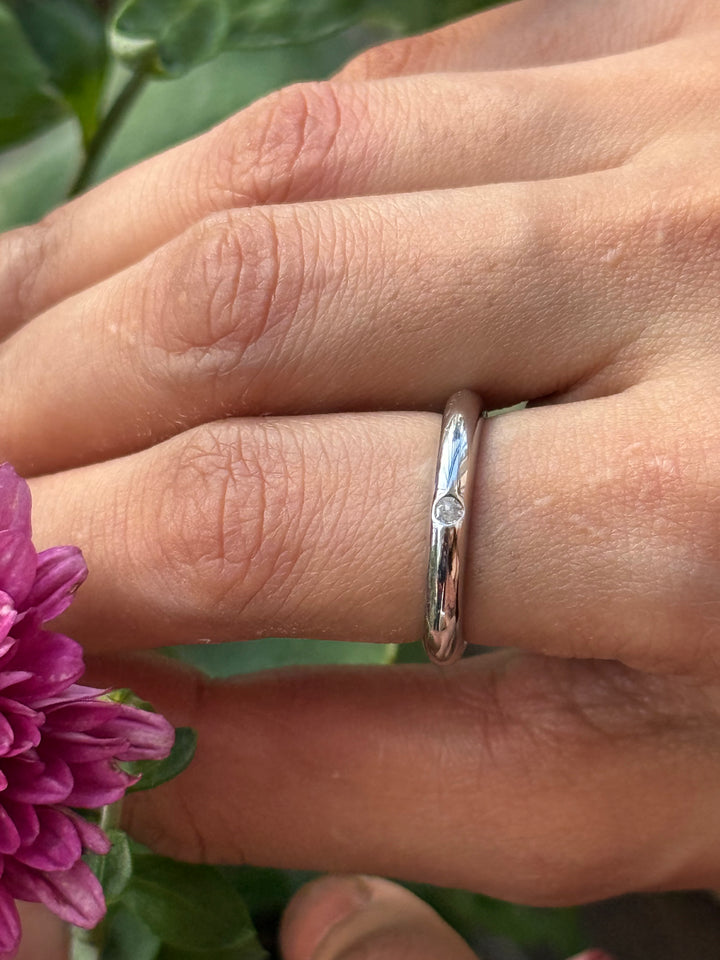 Close-up of a hand wearing a silver ring with a purple flower in the foreground