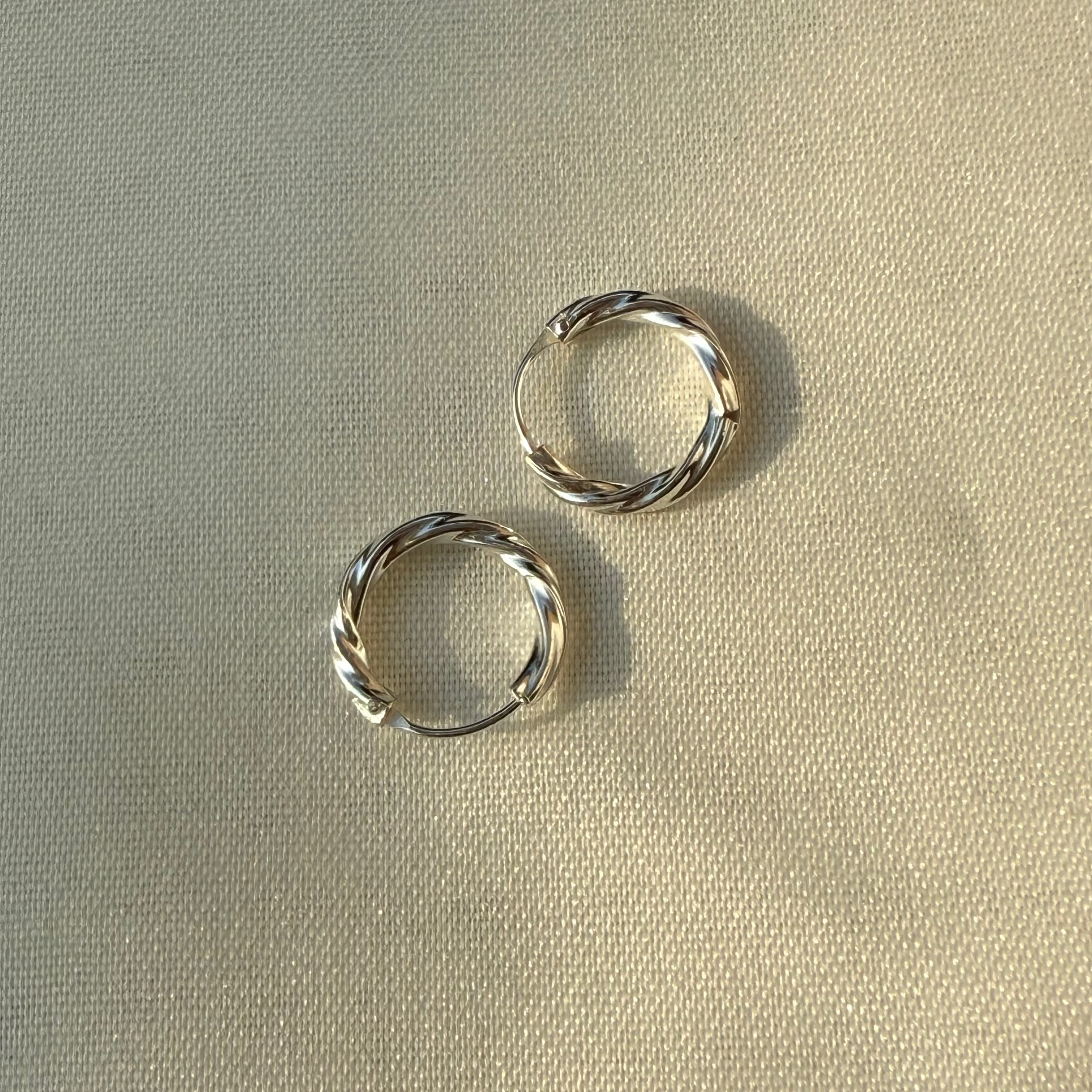 Two silver hoop earrings on a beige fabric background