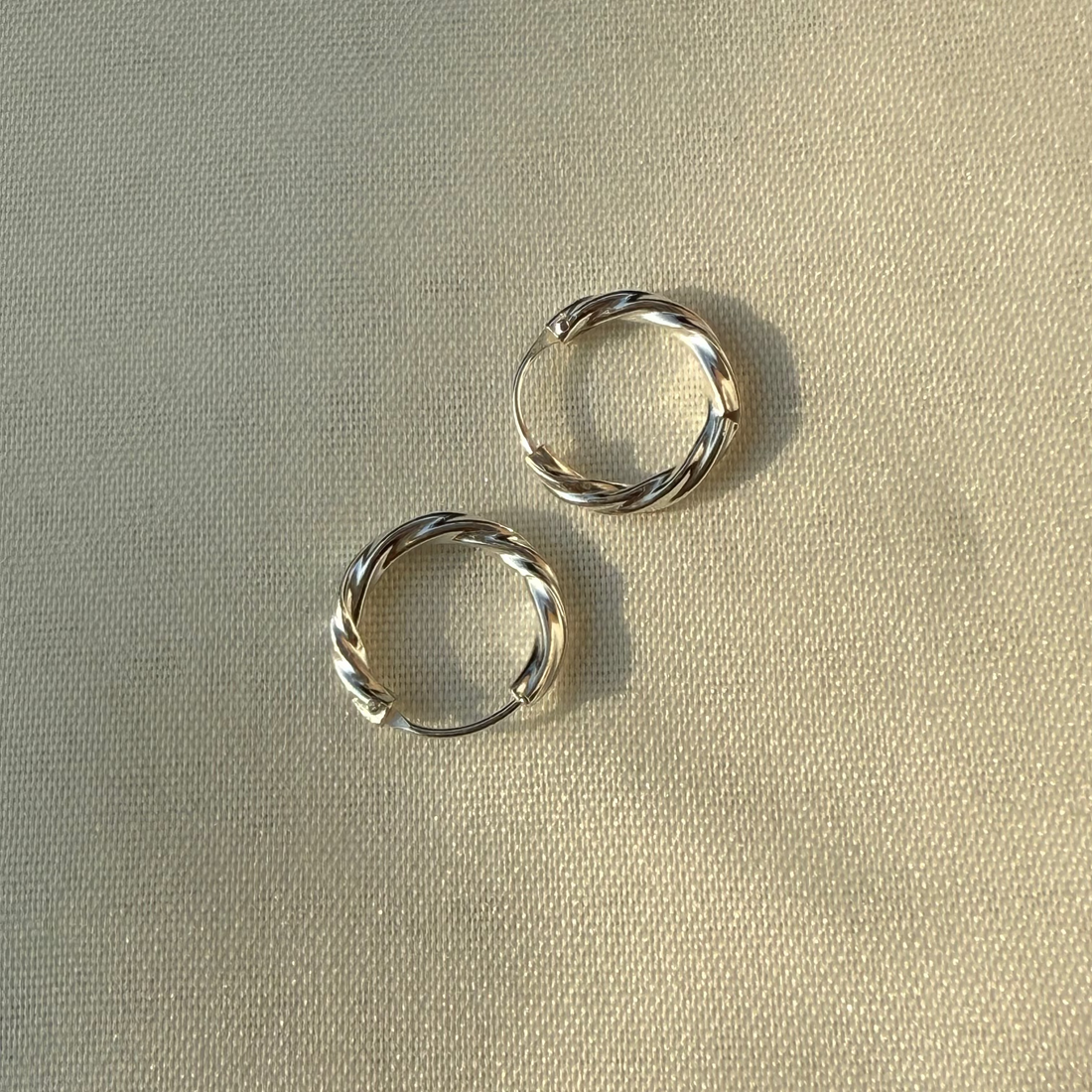 Two silver hoop earrings on a beige fabric background