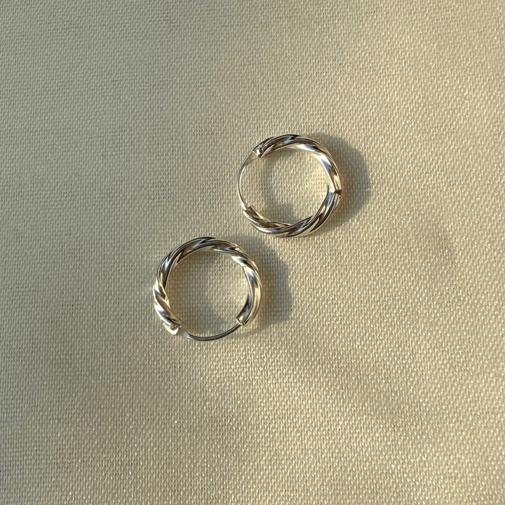 Two silver hoop earrings on a beige fabric background