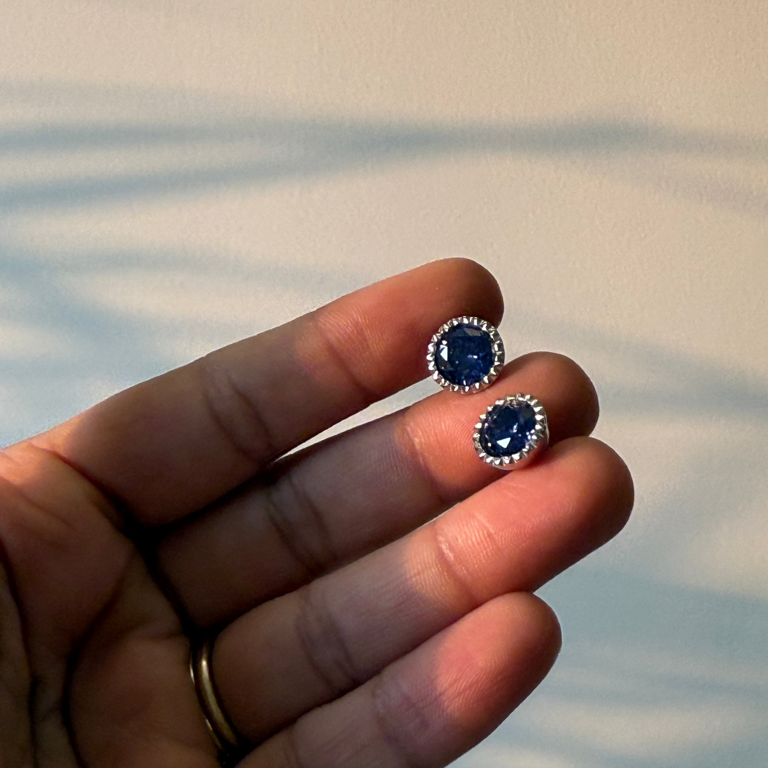 Blue gemstone earrings held between fingers against a neutral background