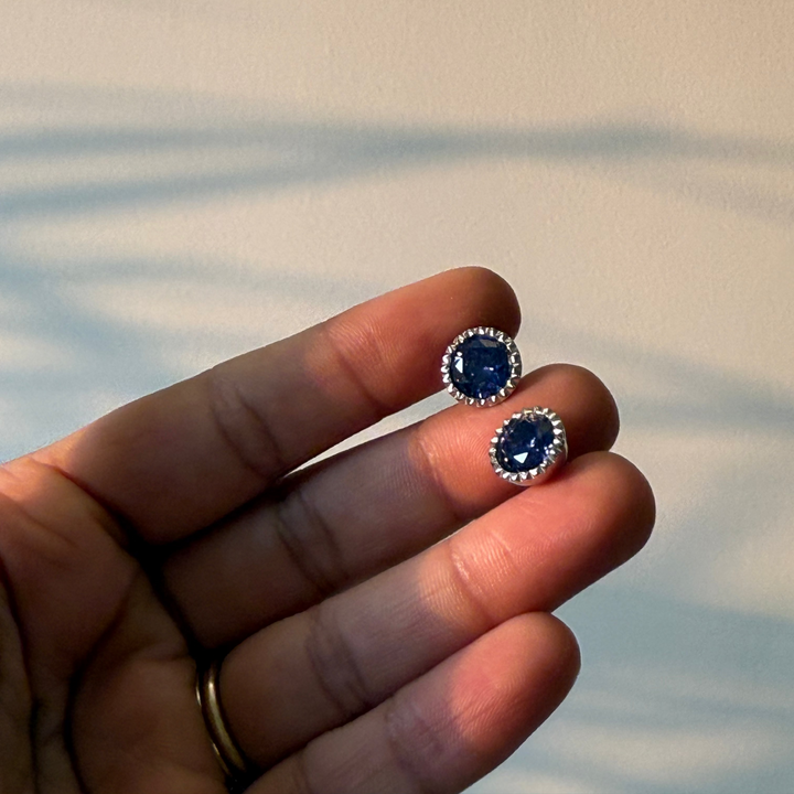 Blue gemstone earrings held between fingers against a neutral background