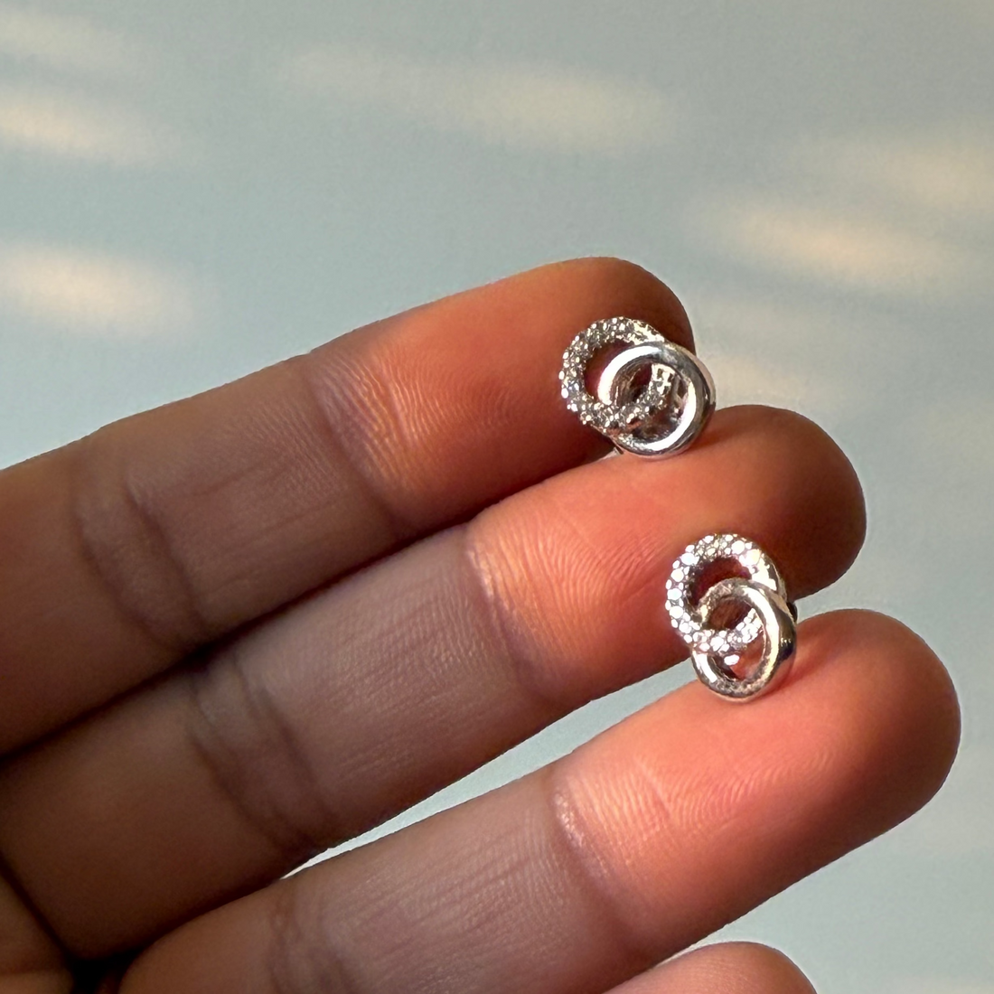 Silver earrings held between fingers against a neutral background