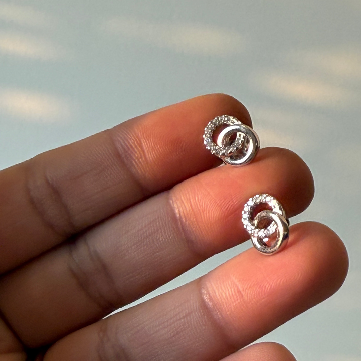 Silver earrings held between fingers against a neutral background