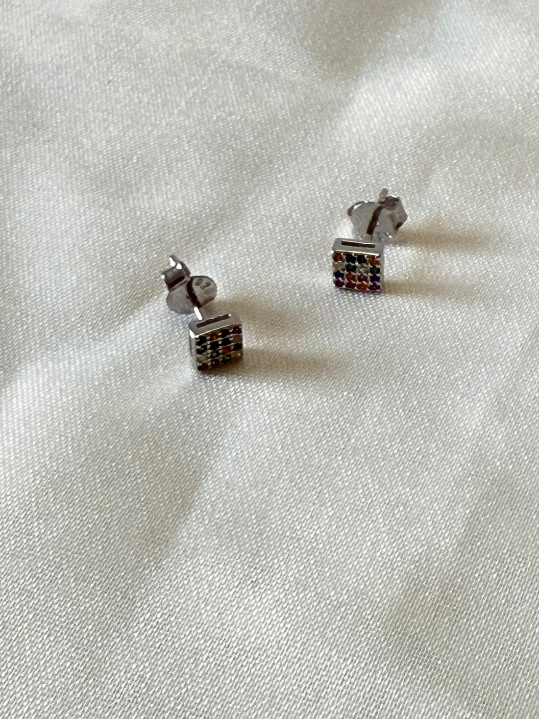 Silver earrings with colorful stones on a light fabric background