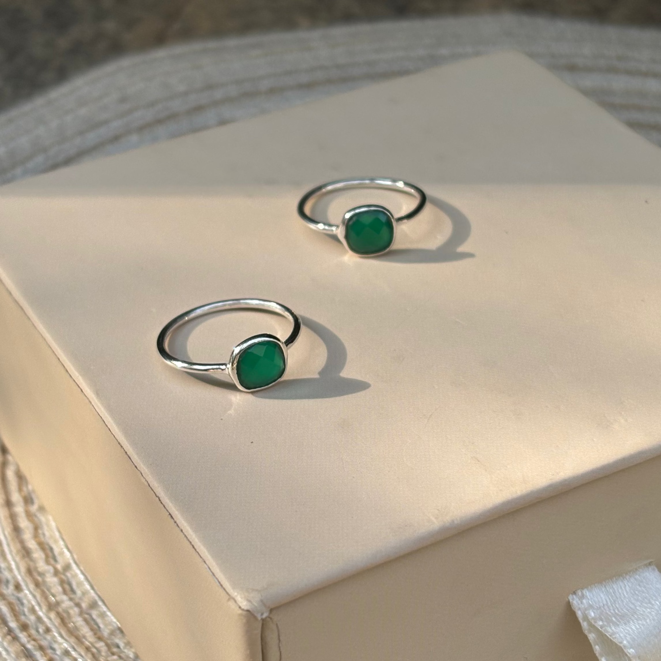 Two silver rings with green gemstones on a beige box.