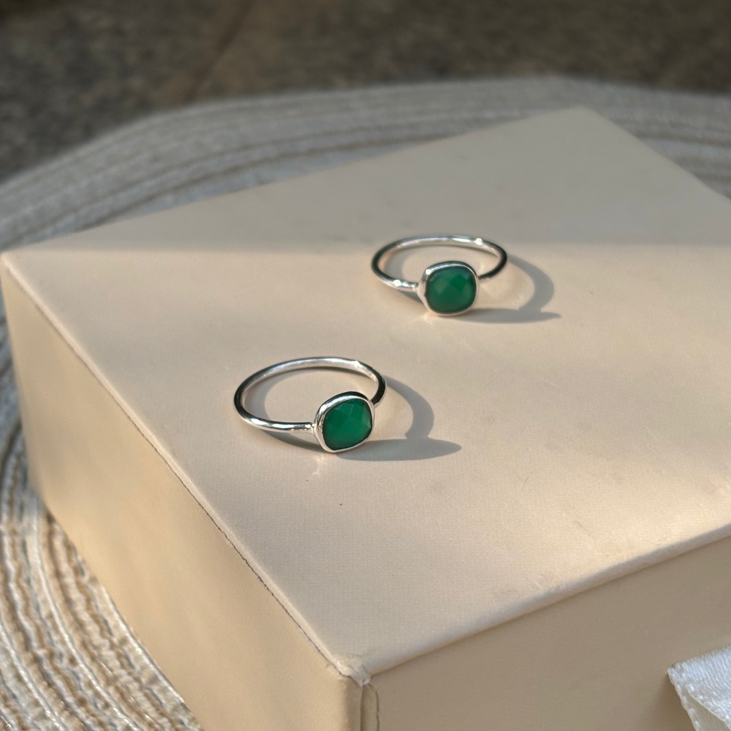 Two green gemstone rings on a beige box with a natural background