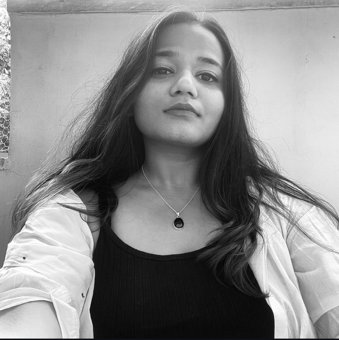 Black and white photo of a person with long hair, wearing a necklace, on a plain background.