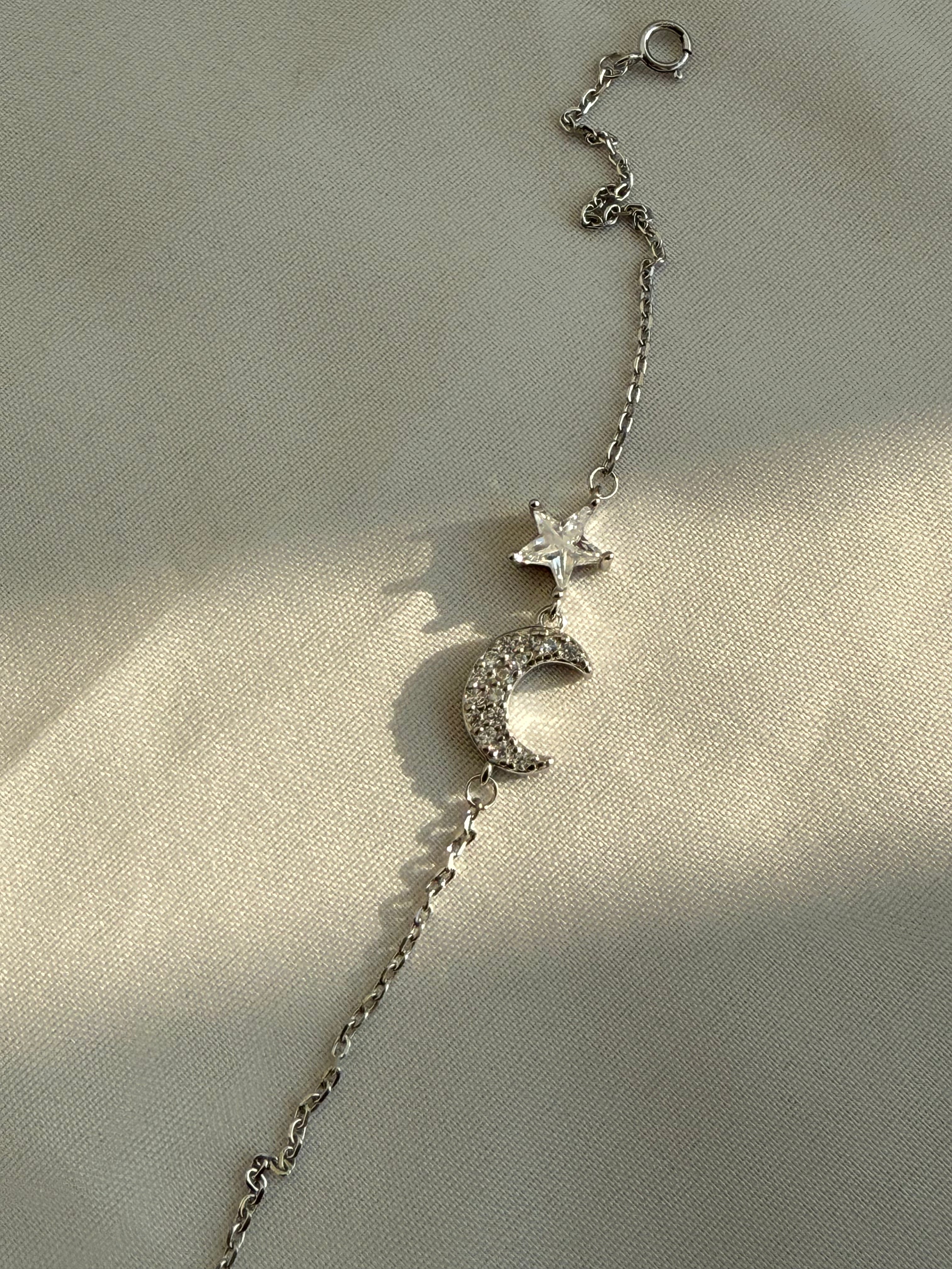 Silver bracelet with star and moon charms on a beige background