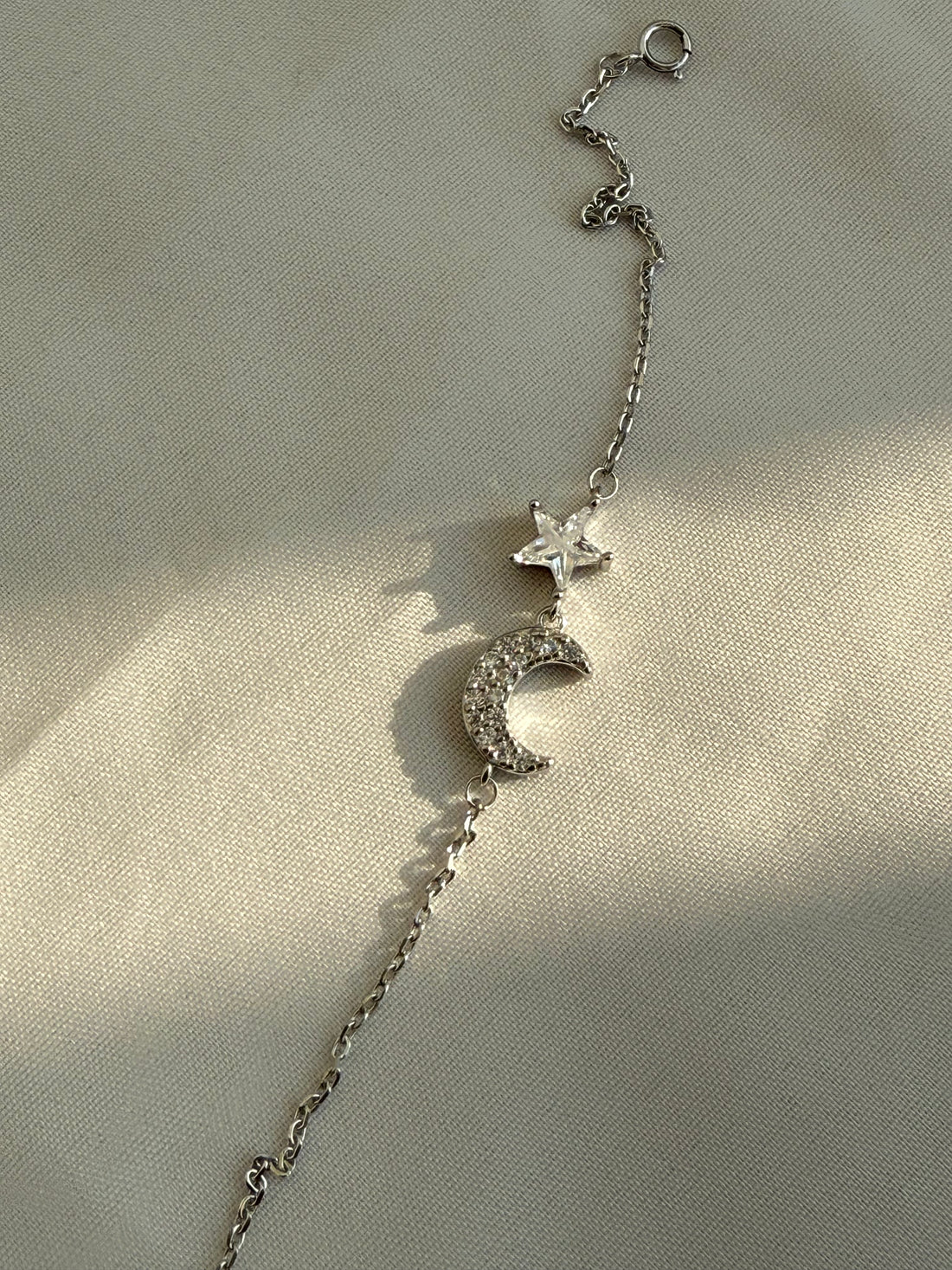 Silver bracelet with star and moon charms on a beige background