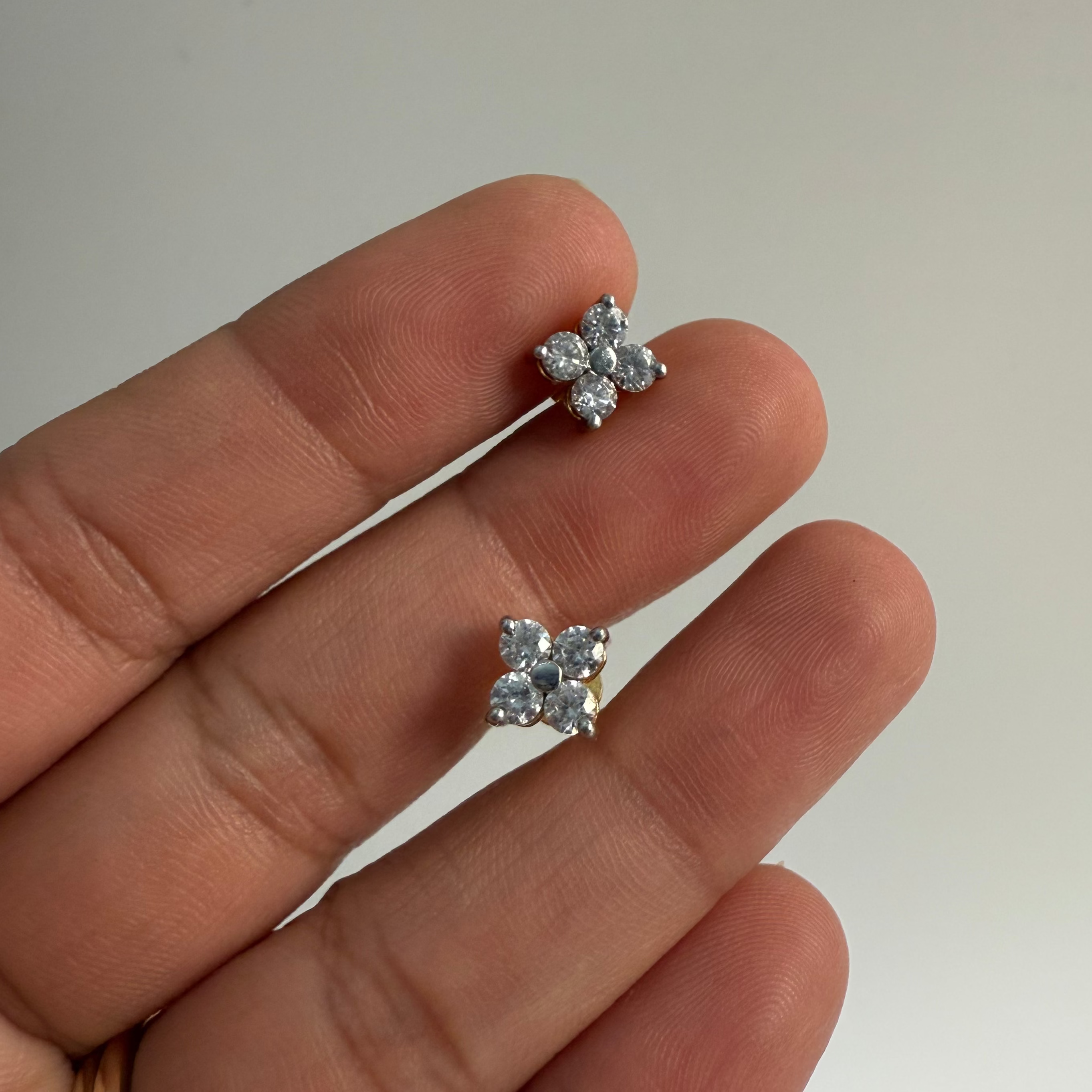 Flower-shaped silver earrings held between fingers against a neutral background