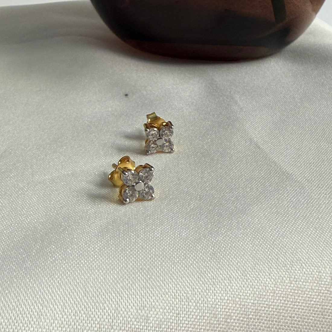 Gold stud earrings with clear gemstones on a light gray fabric background