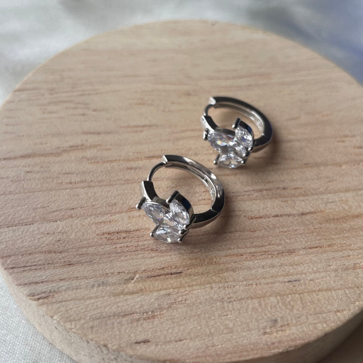 Pair of silver earrings on a wooden stand with a blurred background