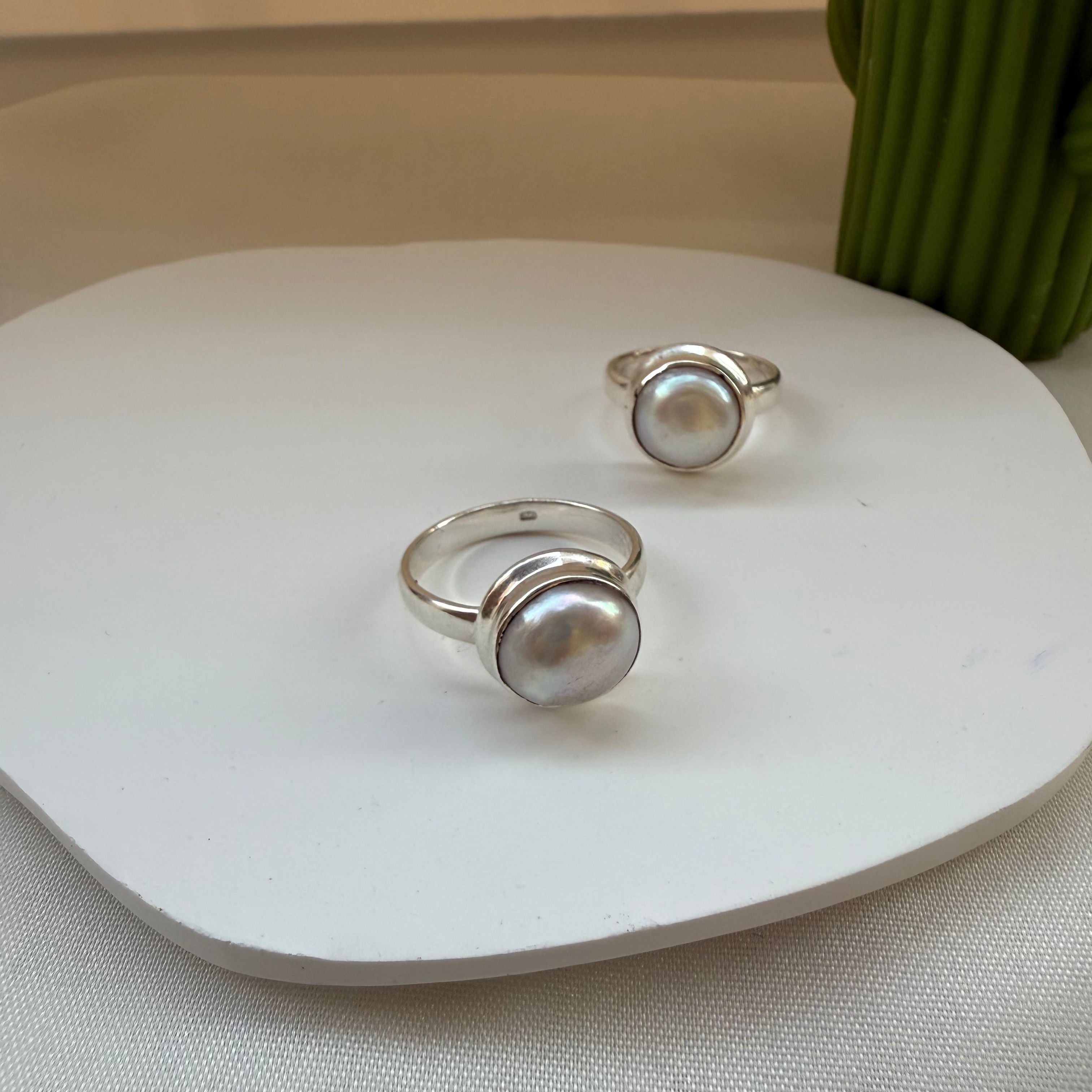 Two silver rings with pearl-like stones on a white surface.