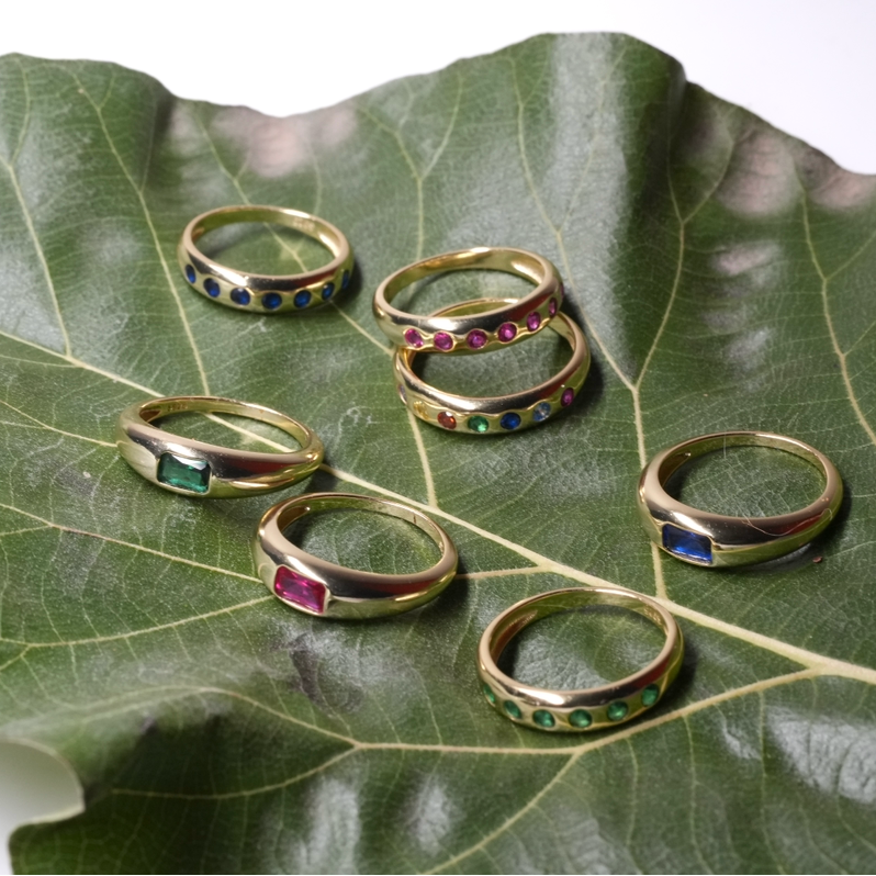 A photo within a phone app showing several gold rings with colorful inlay details resting on a large green leaf. The image has a screenshot header and a row of thumbnail images along the bottom.