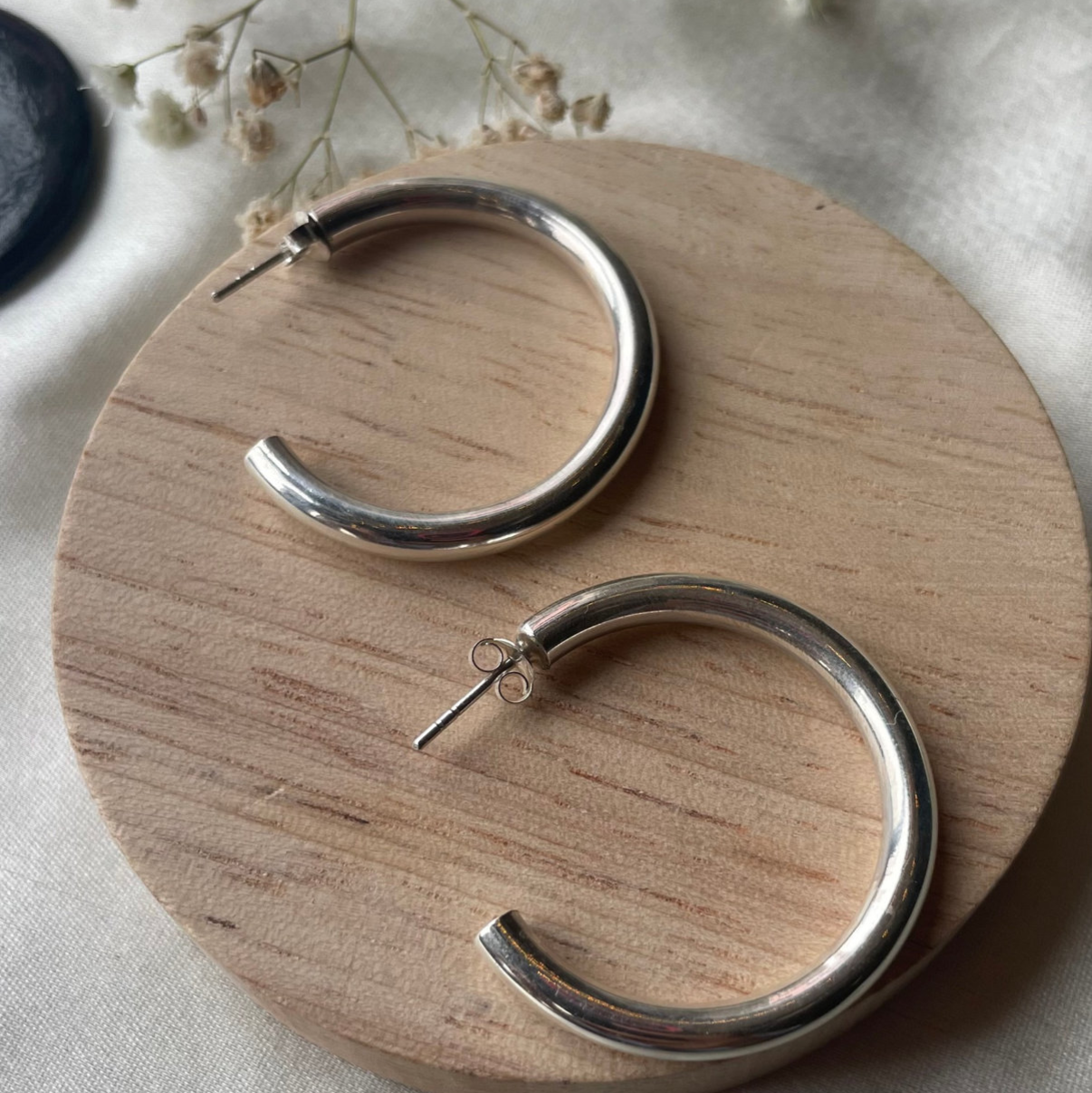 Silver hoop earrings on a wooden stand with dried flowers in the background