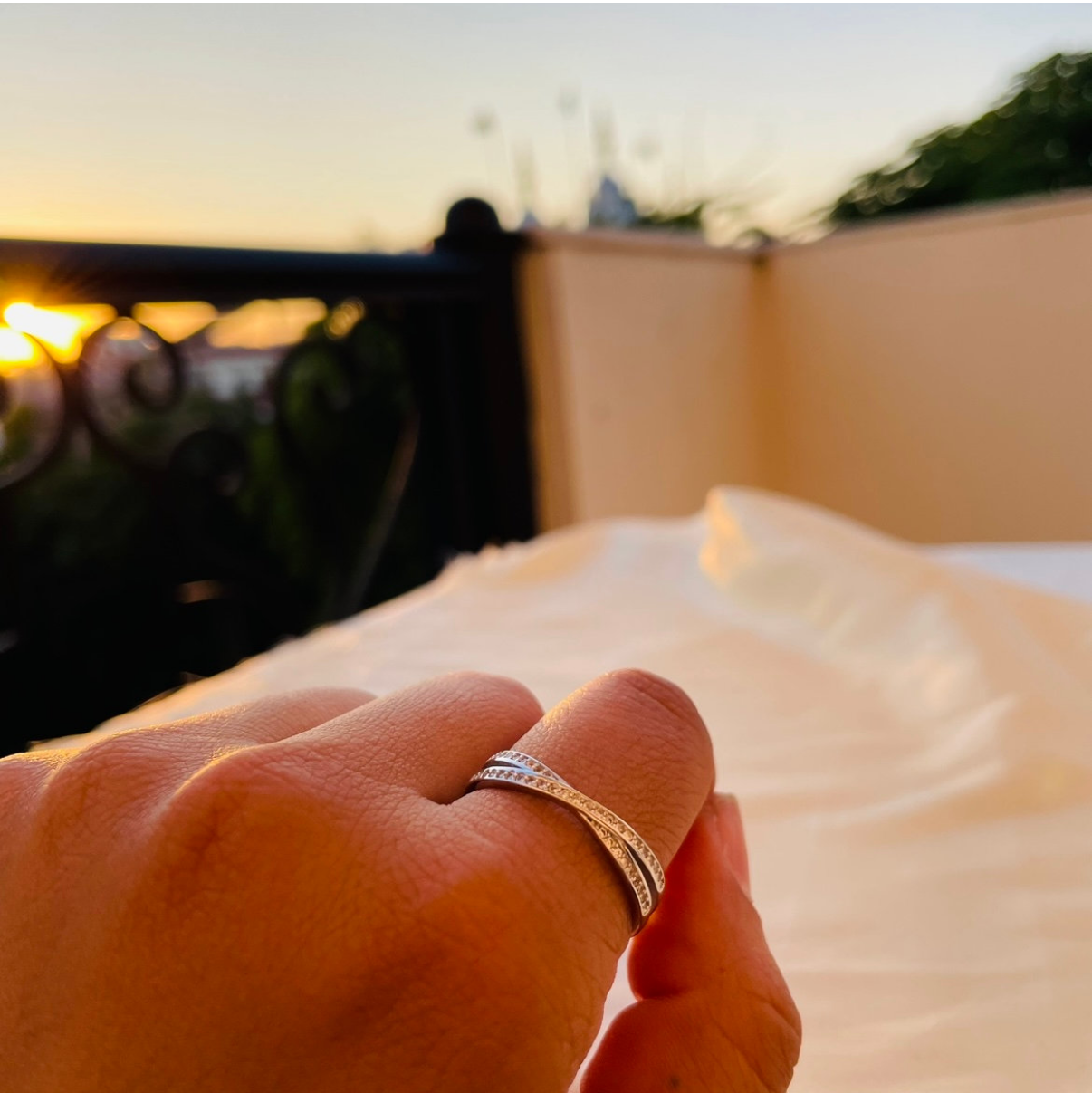Hand holding a ring with a scenic background of a sunset or sunrise.