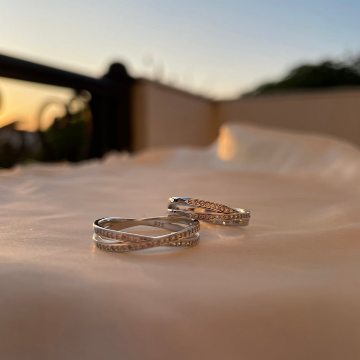 Two silver rings on a reflective surface with a blurred natural background