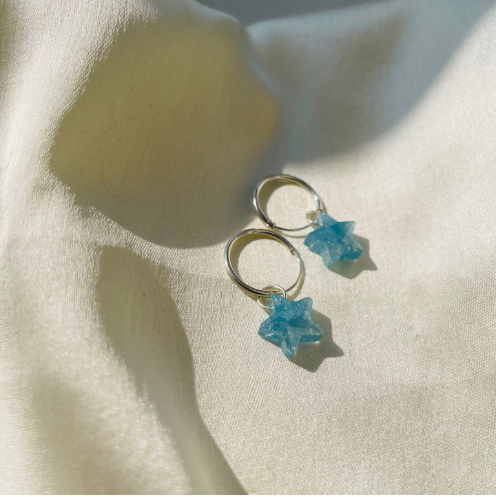 Pair of earrings with blue star-shaped charms on a light fabric background