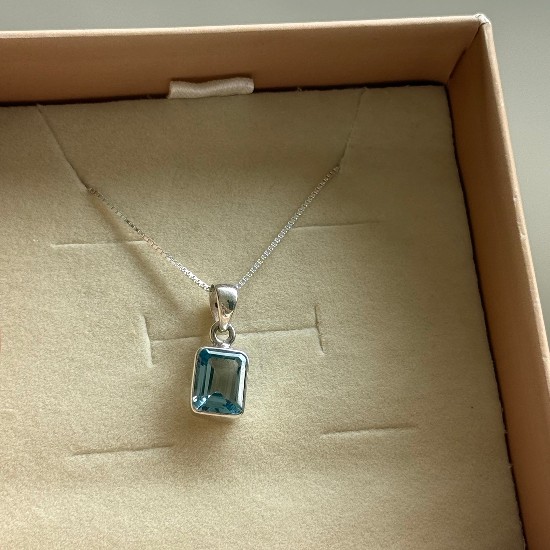 Silver necklace with a blue pendant in an open box