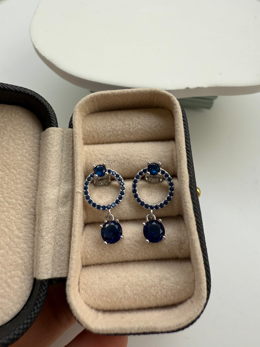Blue gemstone earrings in a beige jewelry box on a white surface