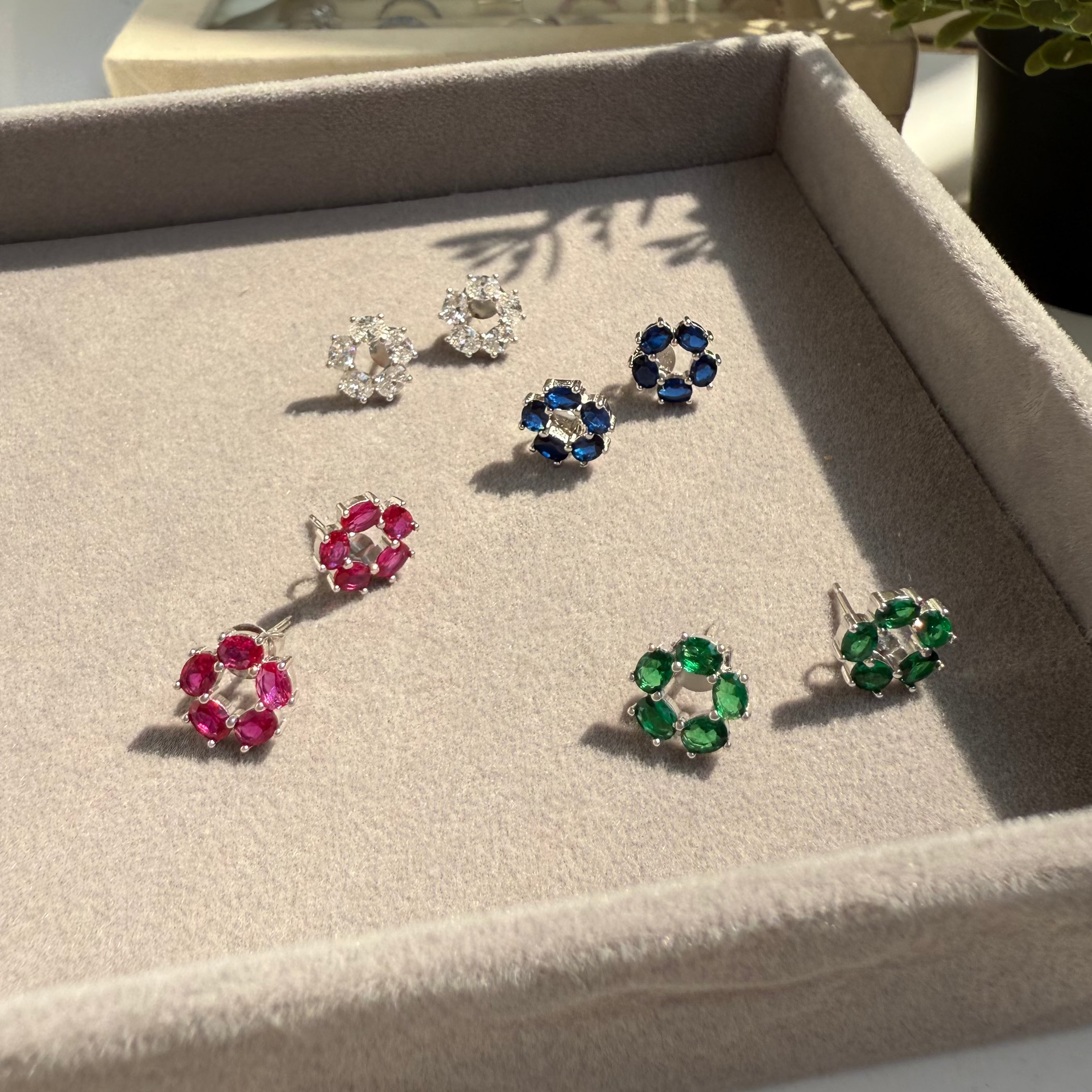 Set of colorful flower-shaped earrings on a display tray with a plant in the background.
