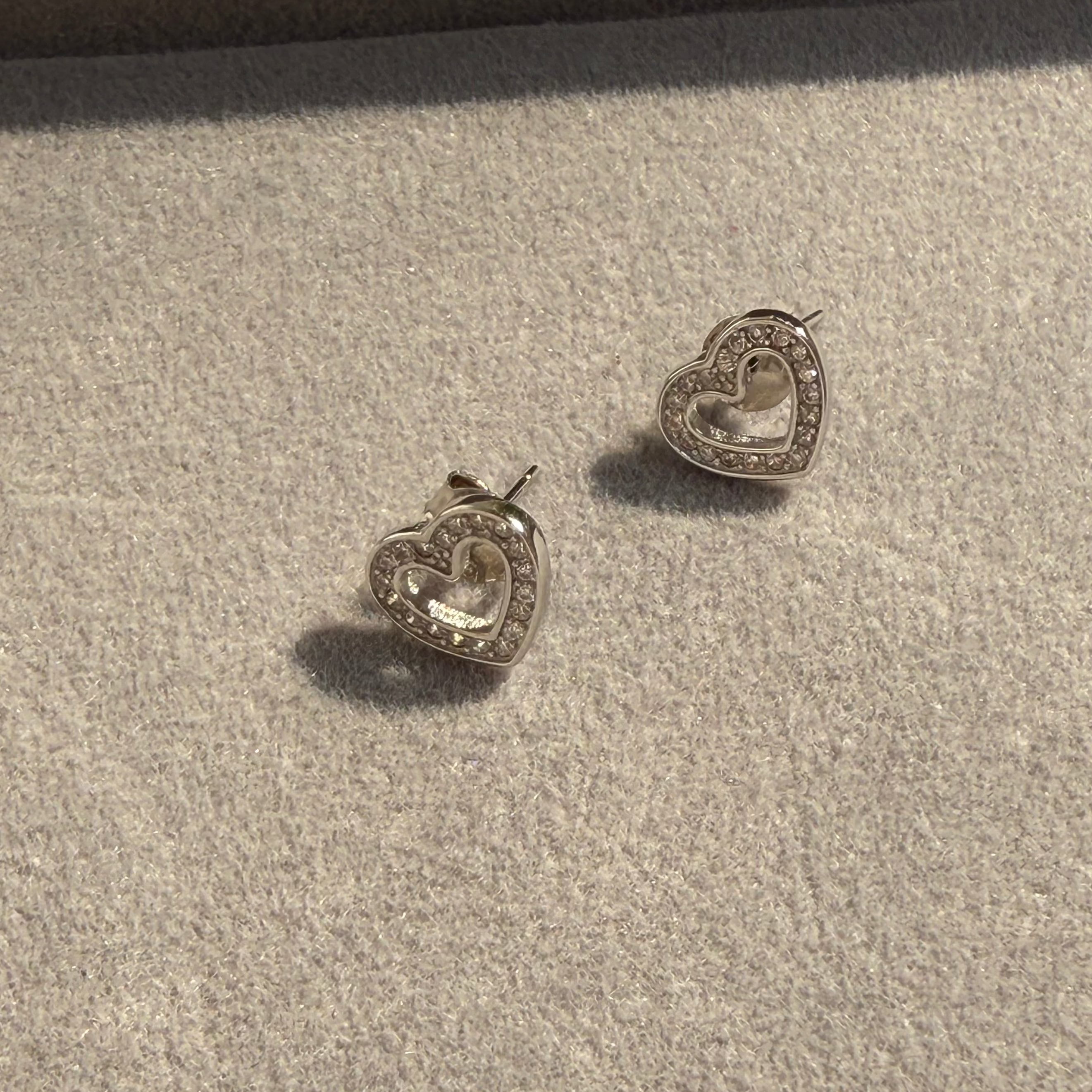 Heart-shaped silver earrings on a textured beige surface