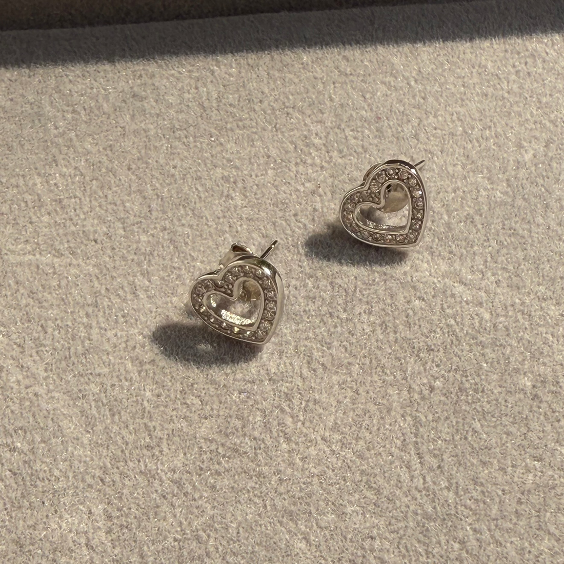 Heart-shaped silver earrings on a textured beige surface