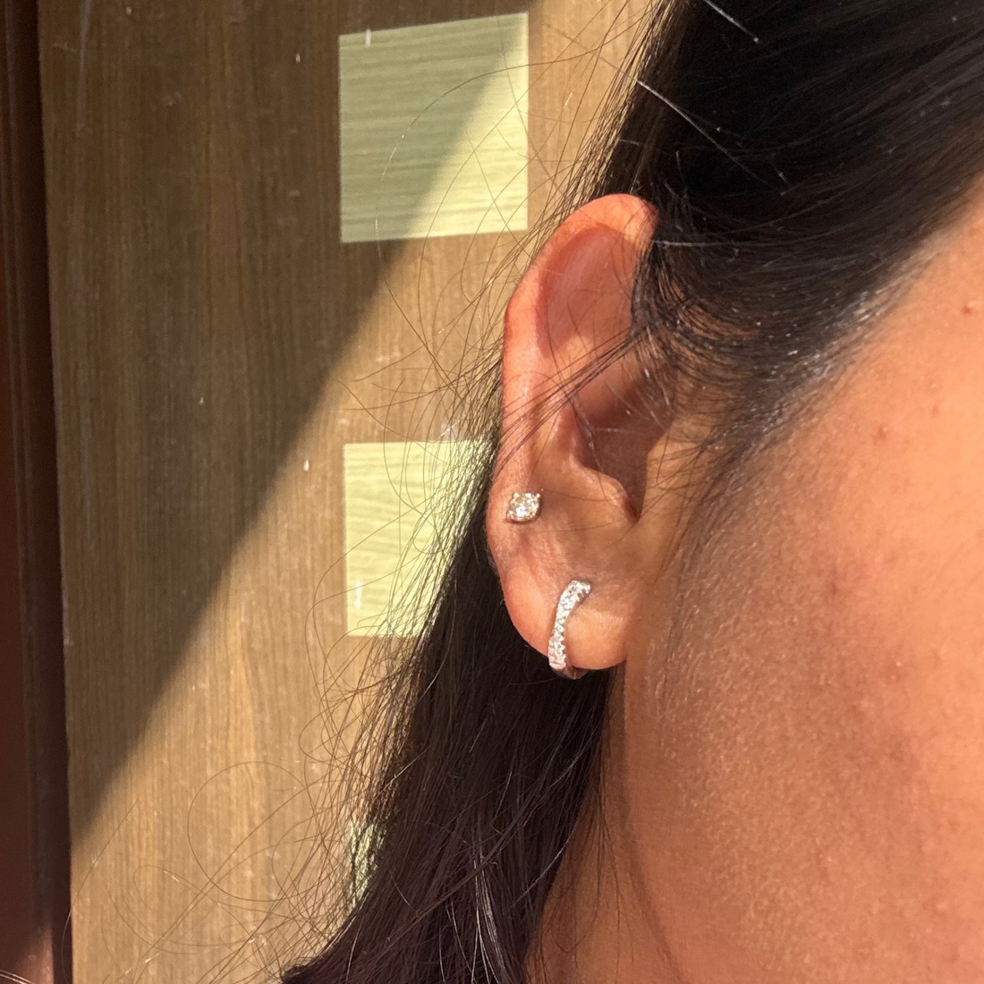 Close-up of a person wearing earrings with a wooden panel background