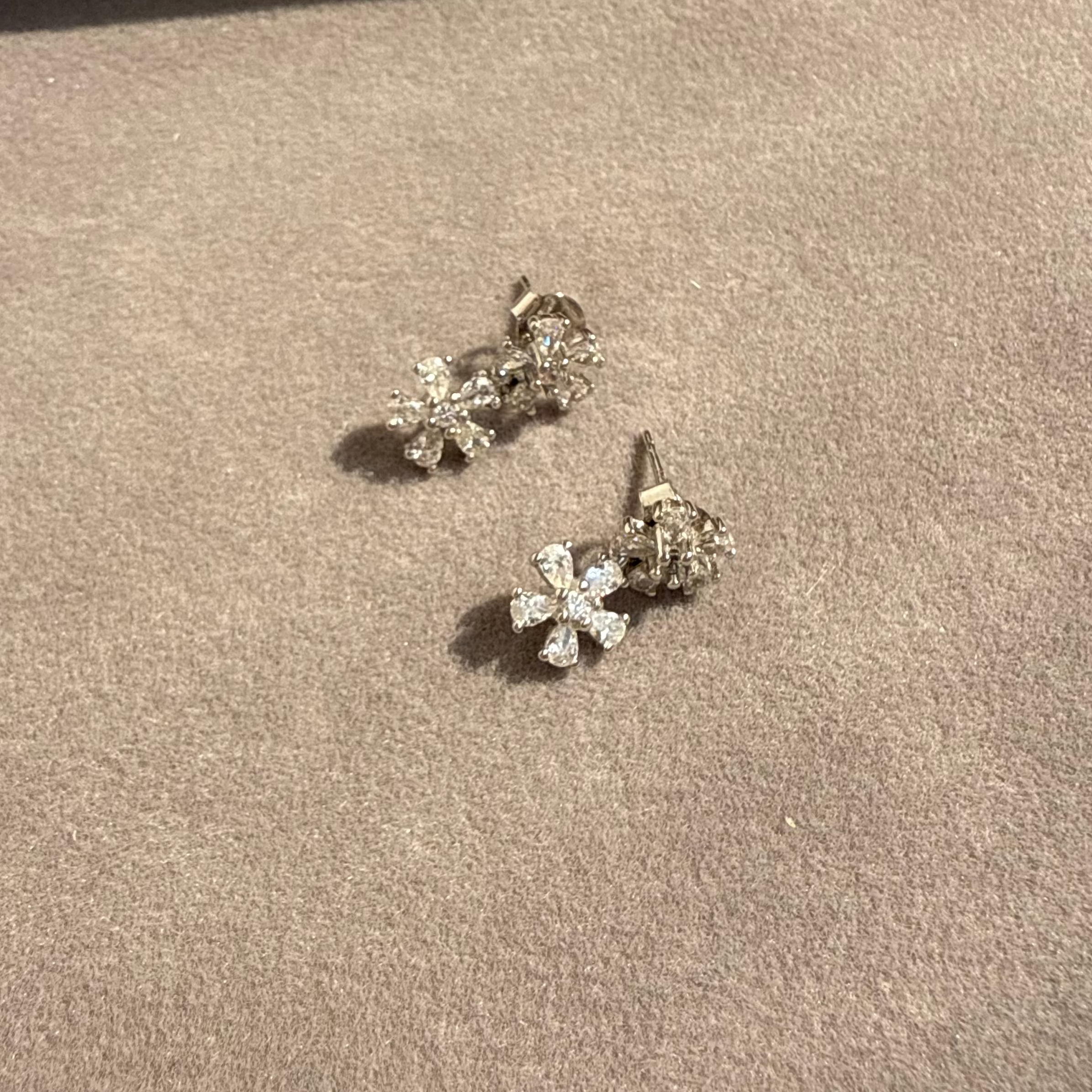 Pair of silver flower-shaped earrings on a brown surface