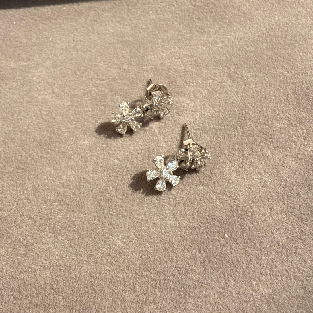 Pair of silver flower-shaped earrings on a brown surface