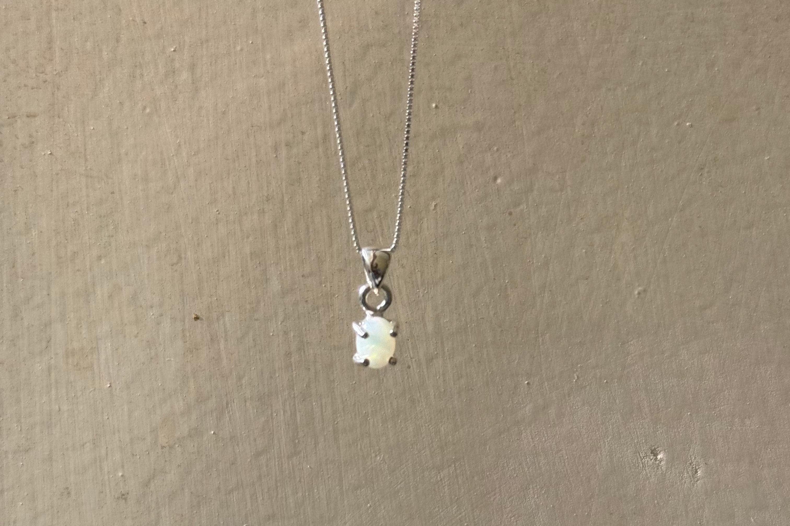 A silver chain necklace with a small white bear-shaped pendant, hanging against a textured beige wall.