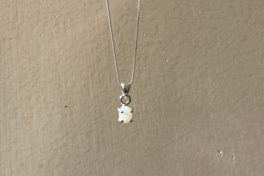 A silver chain necklace with a small white bear-shaped pendant, hanging against a textured beige wall.