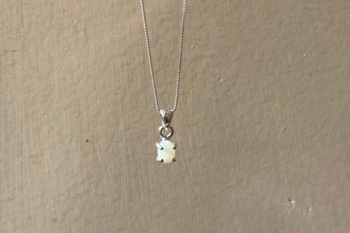 A silver chain necklace with a small white bear-shaped pendant, hanging against a textured beige wall.