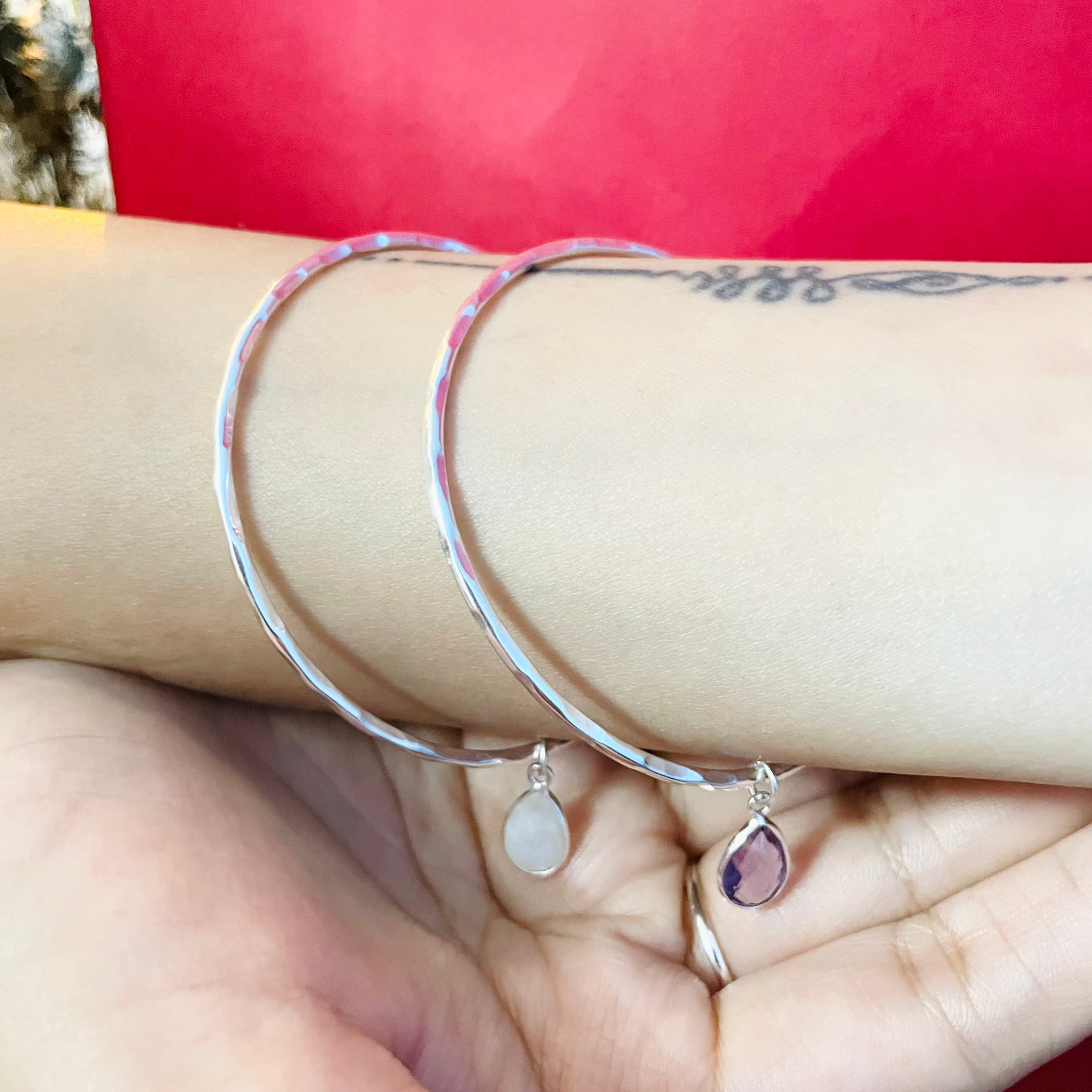 Silver bangles with teardrop-shaped gemstones on a wrist against a red background