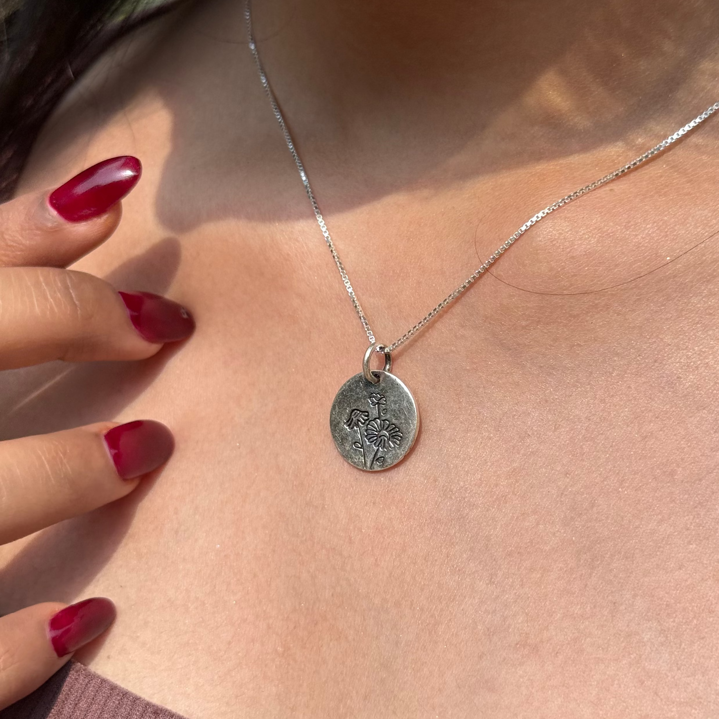 Silver necklace with a pendant worn by a person with red nail polish.