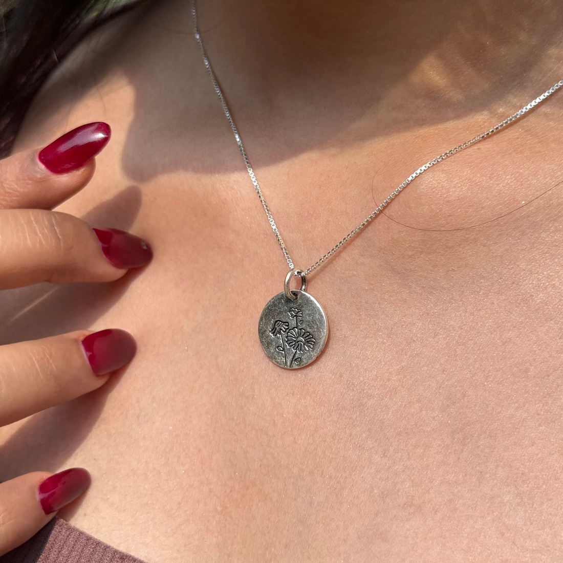 Silver necklace with a pendant worn by a person with red nail polish.