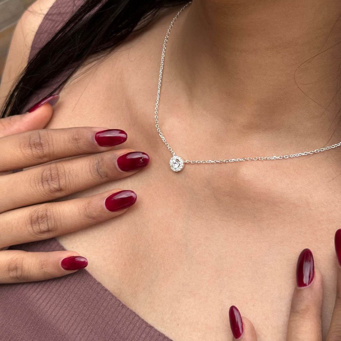 Woman wearing a silver necklace with a diamond pendant, touching her chest.