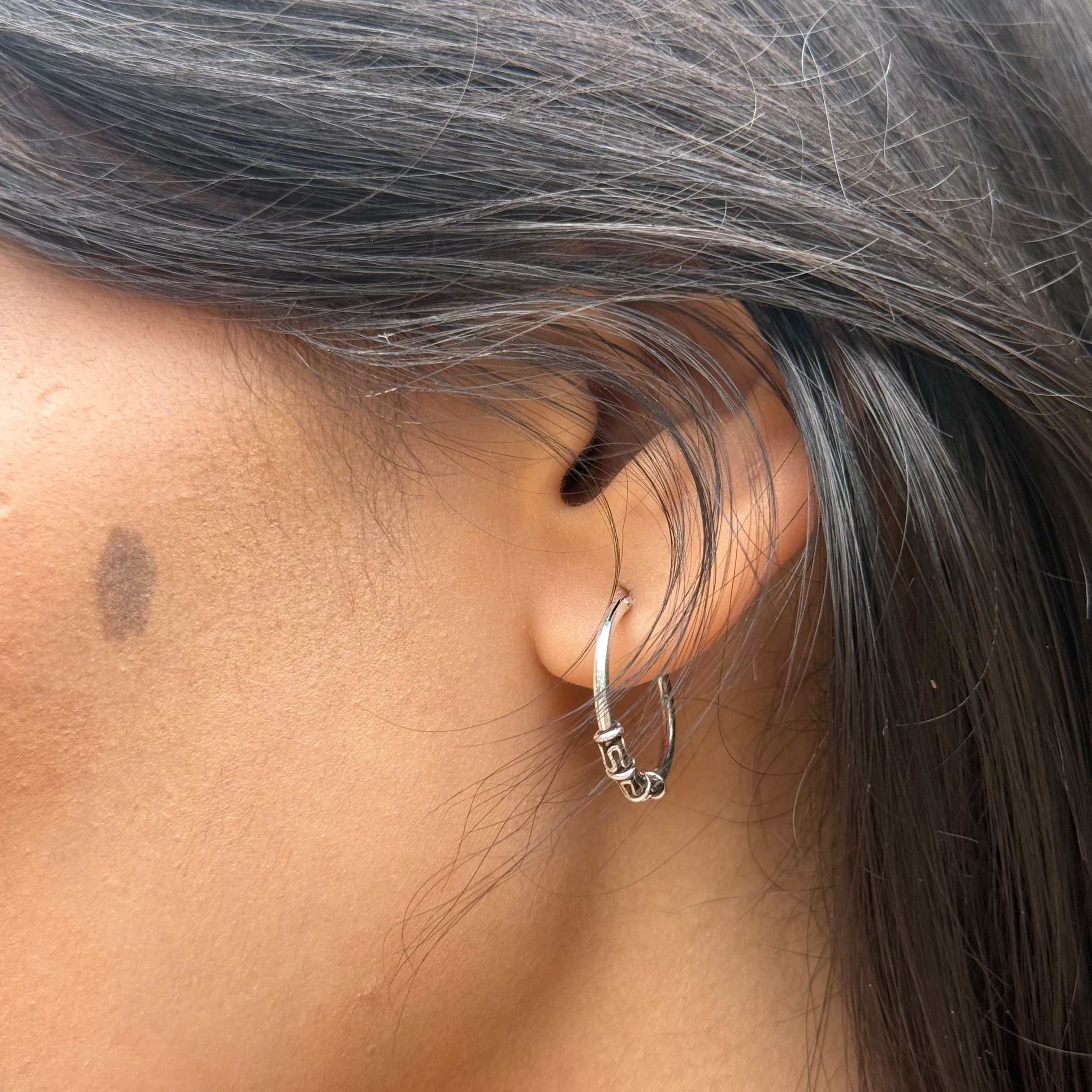 Close-up of an ear with a silver hoop earring and gray hair.