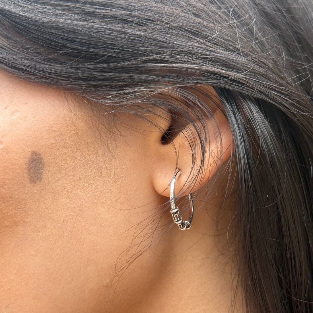 Close-up of an ear with a silver hoop earring and gray hair.