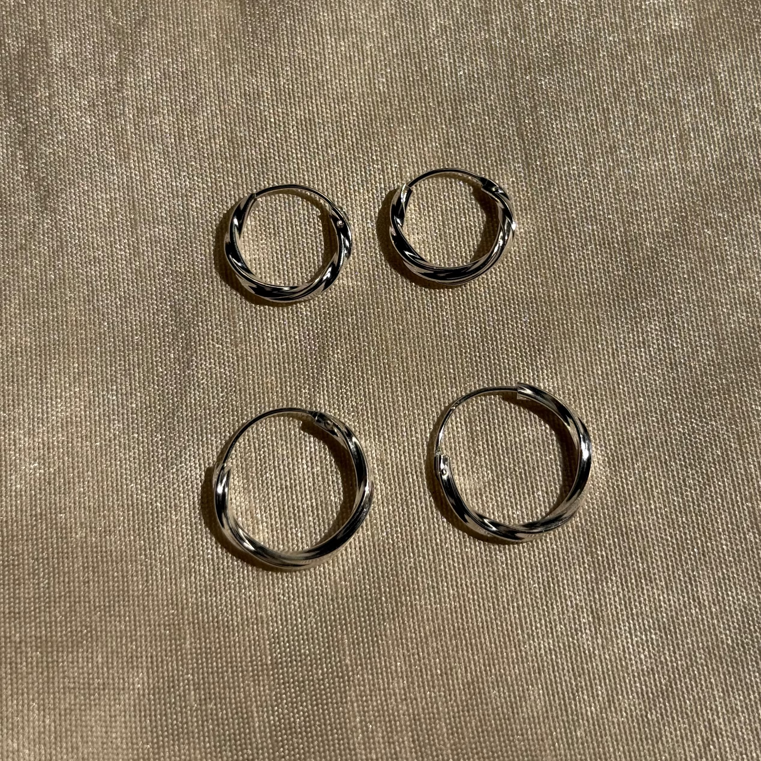 Four silver hoop earrings on a beige fabric background