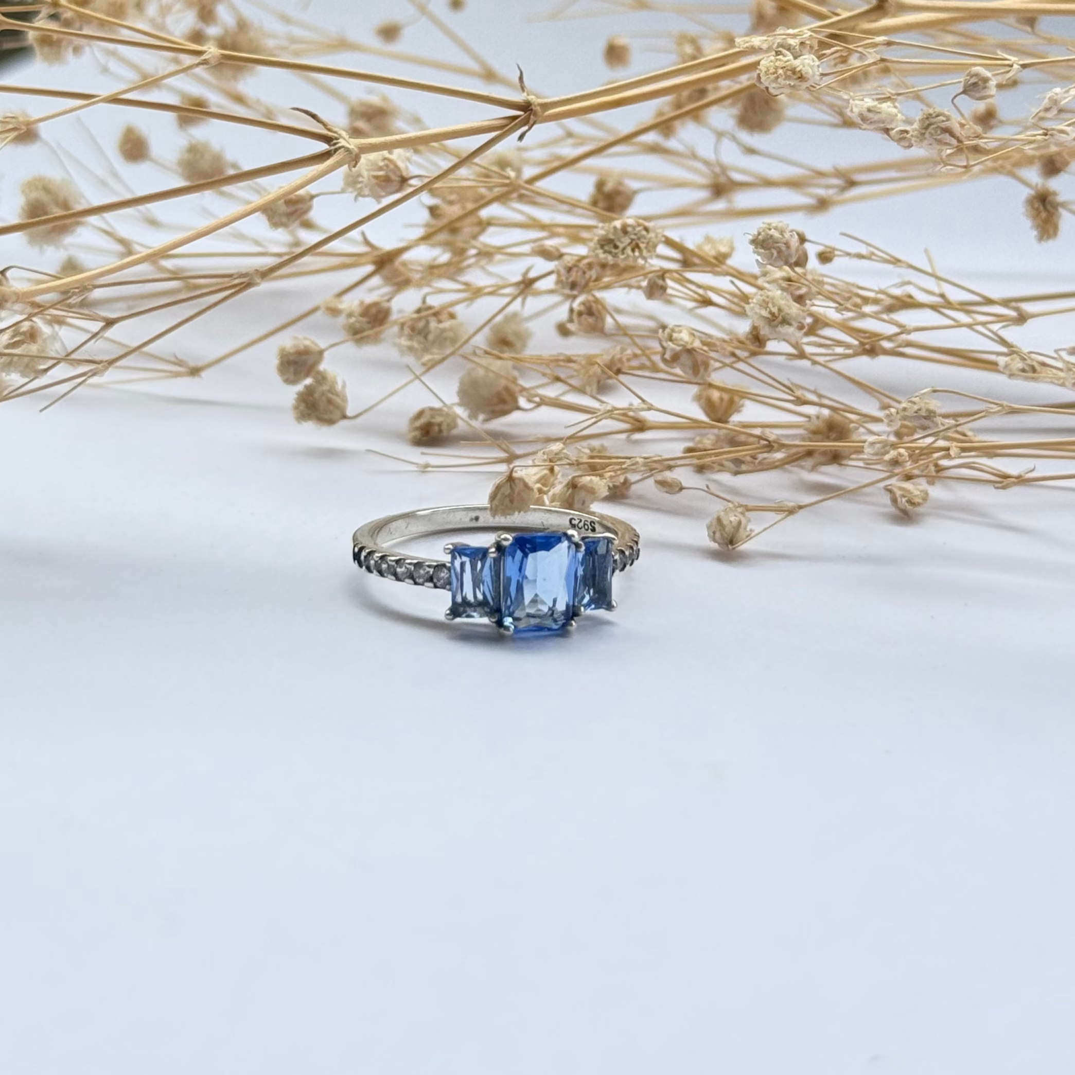 Blue gemstone ring on a light surface with flowers
