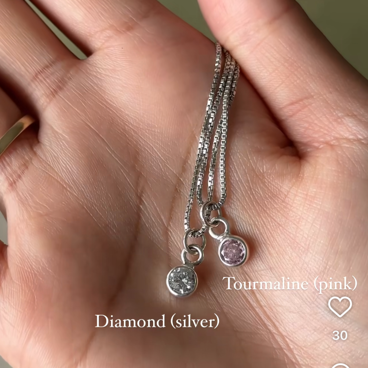 Hand holding two silver necklaces with diamond pendants on a blurred background.
